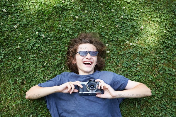 Boy lying in grass with camera
