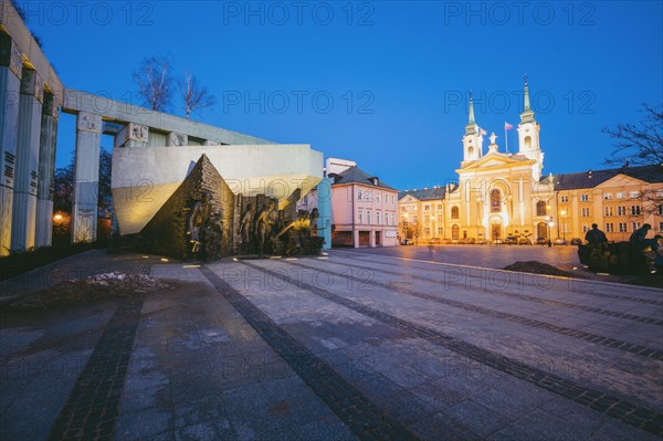 Poland, Masovia, Warsaw, Town square with World War II monument and illuminated cathedral