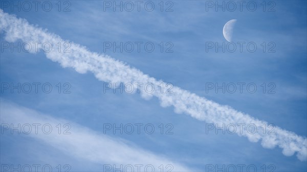 Airplane contrails and waning moon against blue sky