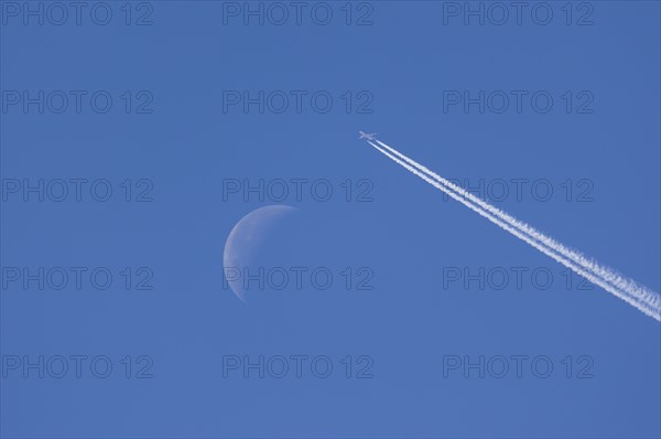 Airplane leaving contrails against blue sky with waning moon