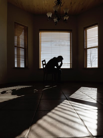 Silhouette of depressed man sitting on chair in living room