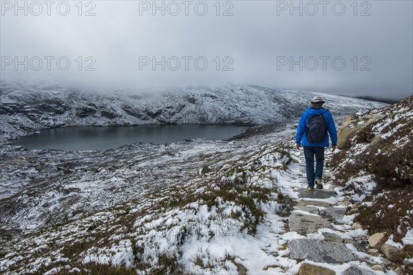 Australia, New South Wales, Woman hiking on snowy trail by lake at Charlotte Pass in Kosciuszko National Park