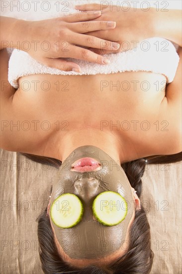 Woman with mud mask and cucumbers on face