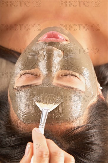 Woman with mud mask and cucumbers on face