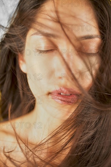 Studio shot of woman with brown tousled hair and eyes closed