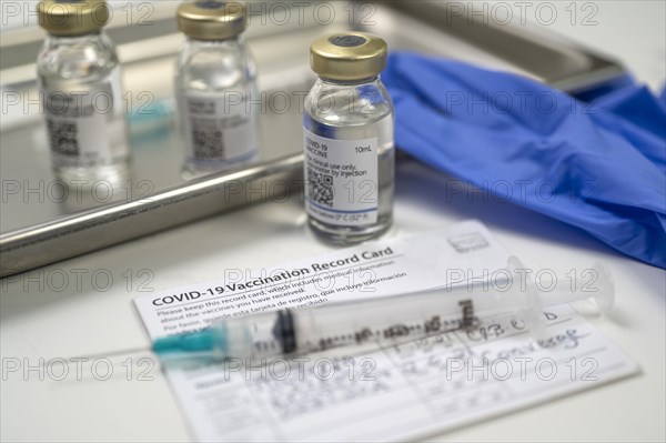 Syringe on Covid-19 vaccination record card and vials on tray