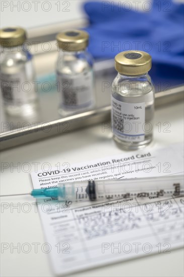 Syringe on Covid-19 vaccination record card and vials on tray