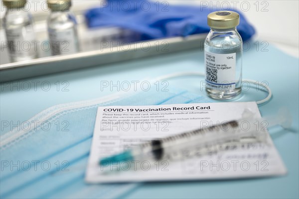 Syringe on Covid-19 vaccination record card and vials on tray