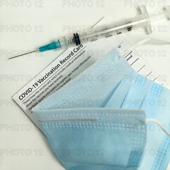 Syringe on Covid-19 vaccination record card and face mask