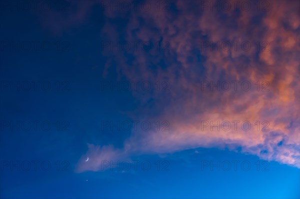 Crescent moon against blue sky with pink clouds