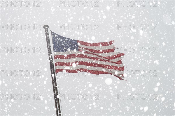 Torn American flag on flag pole with falling snow