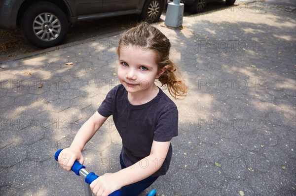 Girl riding push scooter on sidewalk