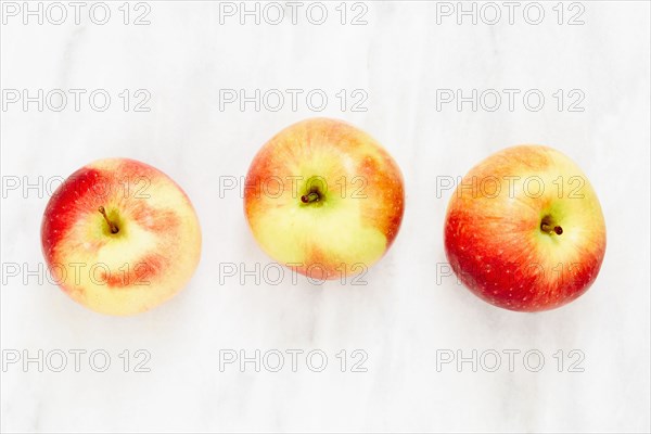 Overhead view of three Gala apples on marble surface