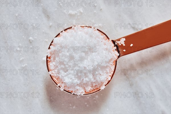 Overhead view of sea salt in measuring spoon on marble surface