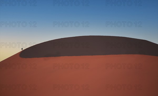Lone man climbing giant sand dune