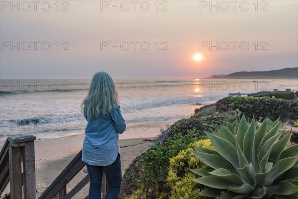 Woman watching sunset from bluff above beach