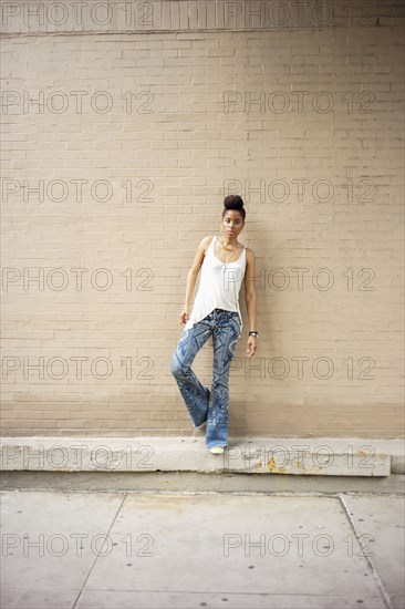 Serious African American woman standing on ledge at brick wall