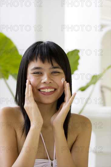 Chinese woman applying moisturizer on face