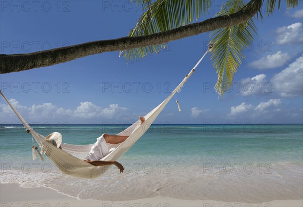 Caucasian woman laying in hammock under palm tree on tropical beach