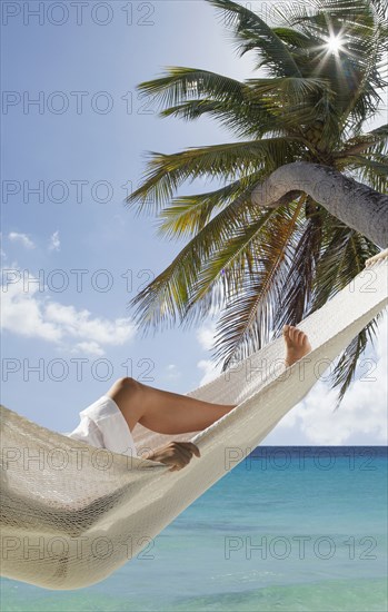 Caucasian woman laying in hammock under palm tree near ocean