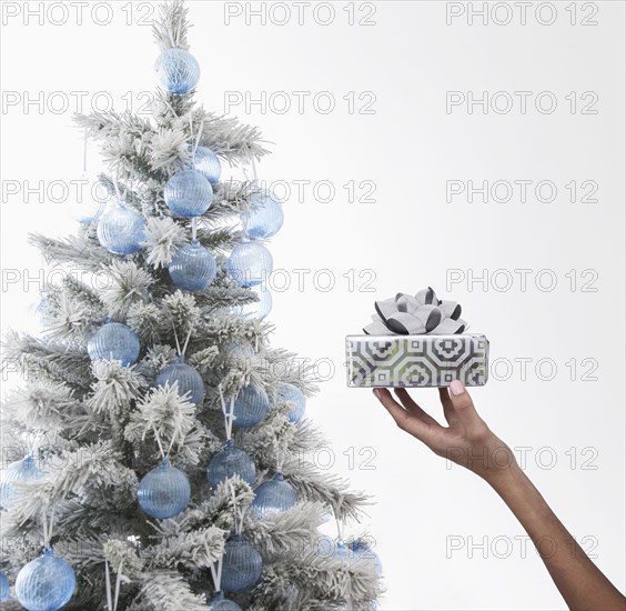 Caucasian woman holding wrapped gift near Christmas tree