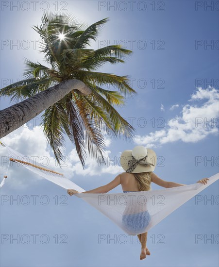 Caucasian woman sitting in hammock under palm tree