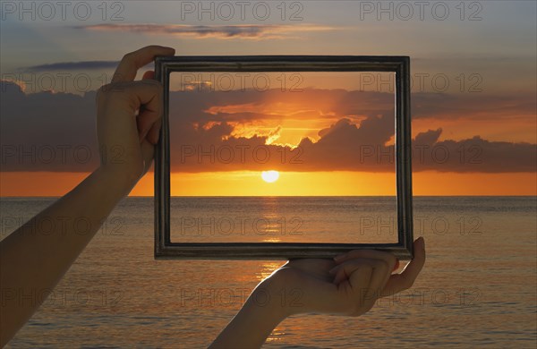 Caucasian woman holding frame over dramatic sunset sky and ocean