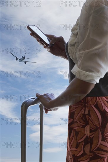 Chinese traveler using cell phone under airplane in blue sky