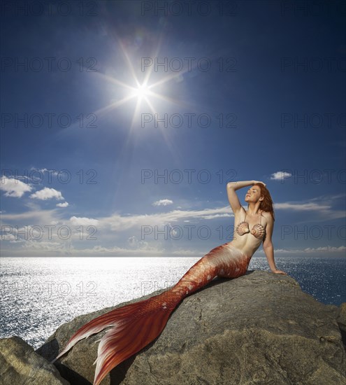 Caucasian mermaid laying on rock near ocean