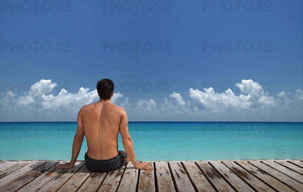 Caucasian man sitting on wooden dock at ocean