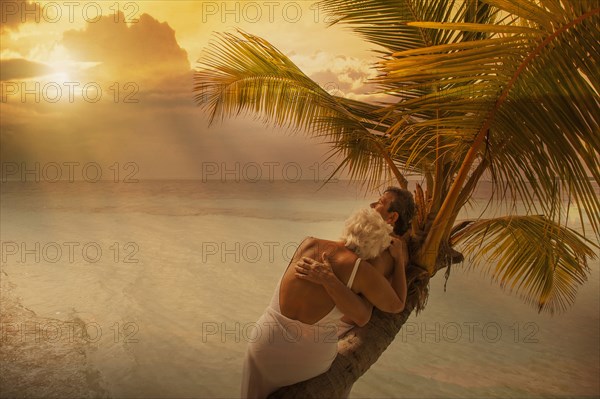 Older Caucasian couple hugging on palm tree at beach