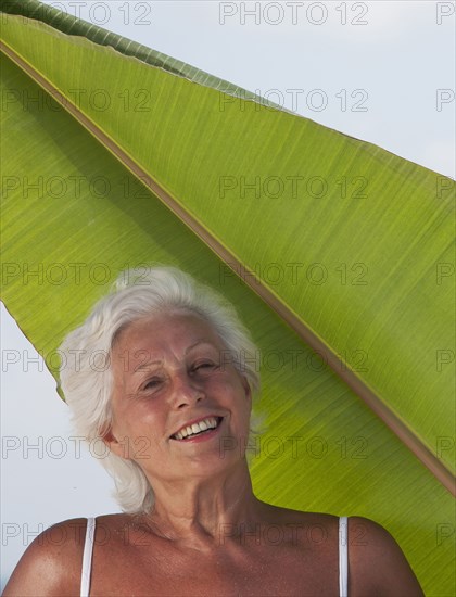 Older Caucasian woman standing under leaf