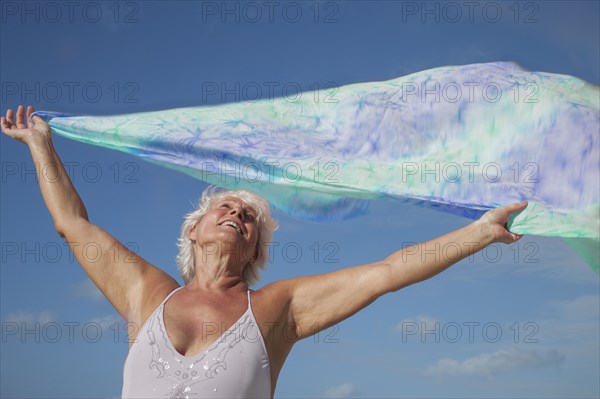 Older Caucasian woman holding fabric in wind under blue sky