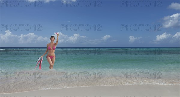Caucasian woman wading on beach with flippers and snorkel