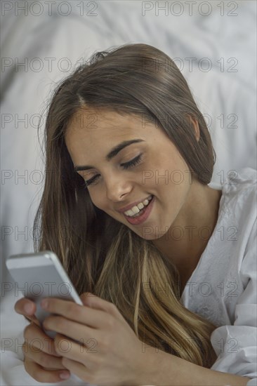 Caucasian woman using cell phone in bed