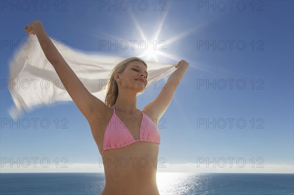 Caucasian woman in bikini holding fabric at beach