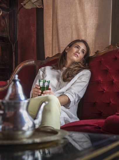 Pensive Caucasian woman sitting on sofa holding cup