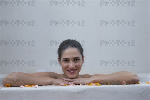 Smiling Caucasian woman in bathtub with flower petals
