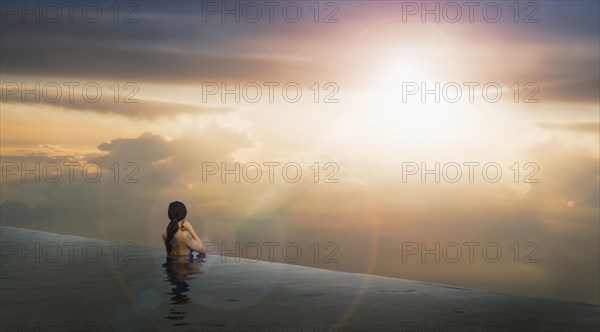 Chinese woman in infinity pool admiring sunset