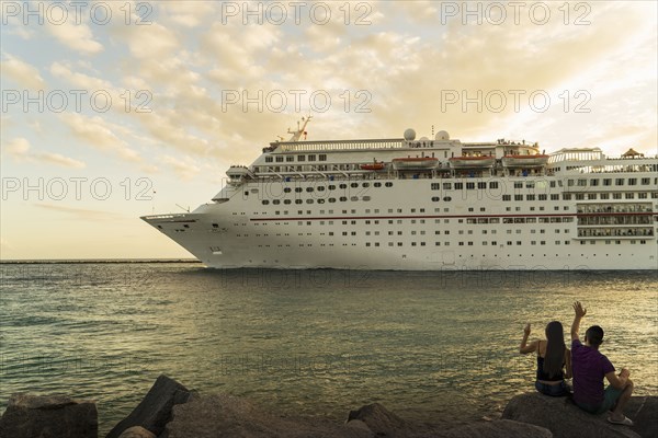 Couple sitting on rocks at river waving to cruise ship