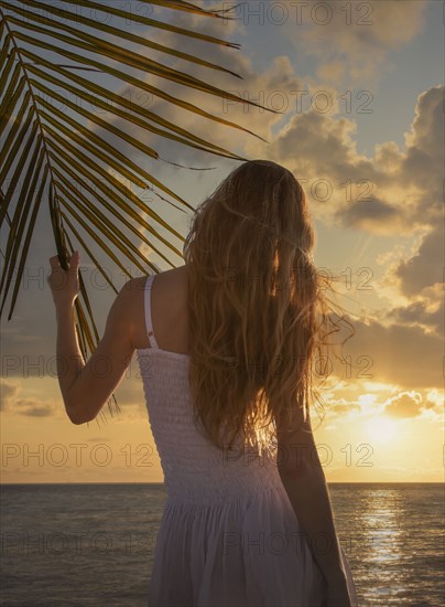 Caucasian woman holding leaf of palm tree near ocean