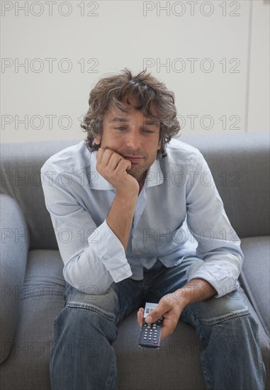 Bored Caucasian man sitting on sofa watching television