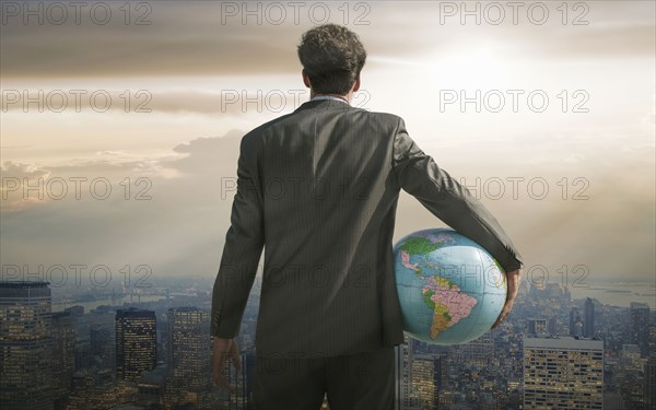 Caucasian businessman holding globe overlooking cityscape