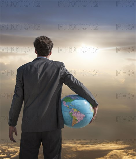 Caucasian businessman holding globe admiring sunset sky