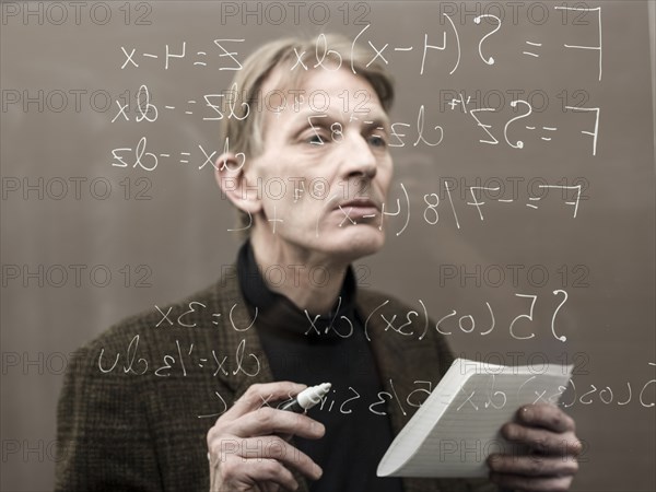 Caucasian teacher looking at formula on glass wall