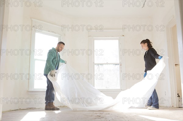 Mixed race couple spreading tarp in new home