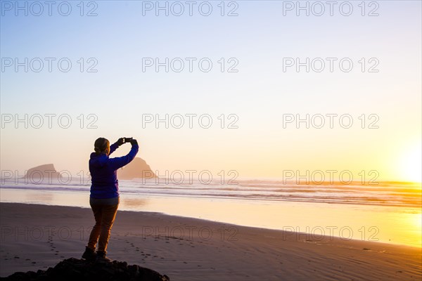 Caucasian woman taking picture of sunrise on beach
