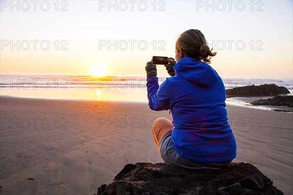 Caucasian woman taking picture of sunrise on beach