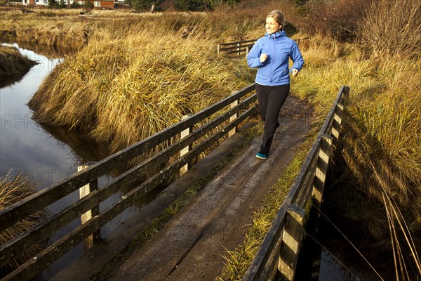 Caucasian woman jogging on wood bridge over creek