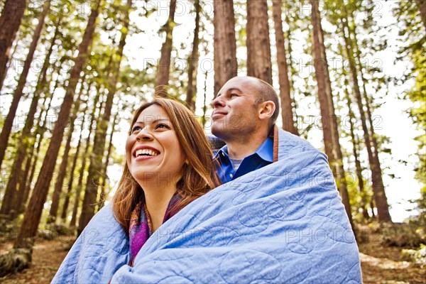 Hispanic couple wrapped in blanket in forest